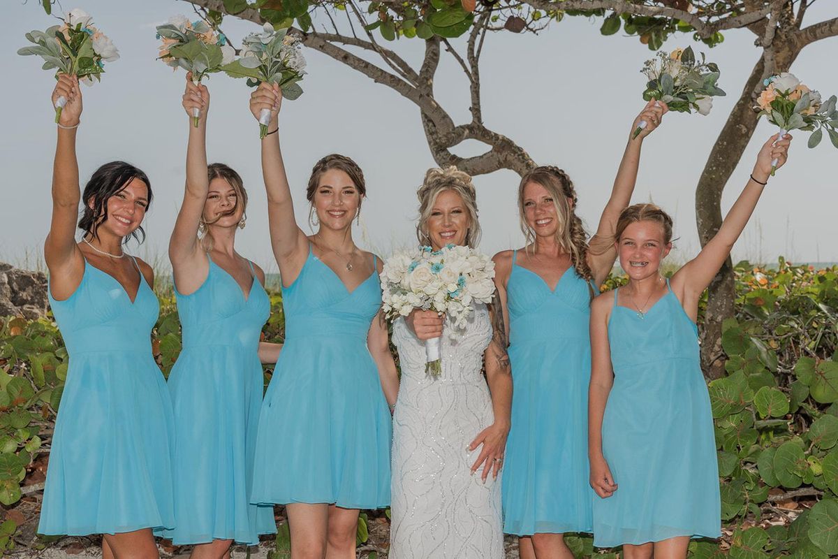 A bride and her bridesmaids in aqua dresses raise their bouquets in celebration