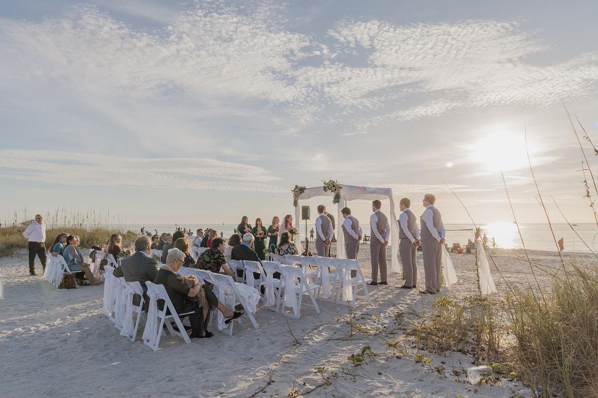 Guests seated in white chairs for a beach wedding ceremony facing the Gulf at golden hour