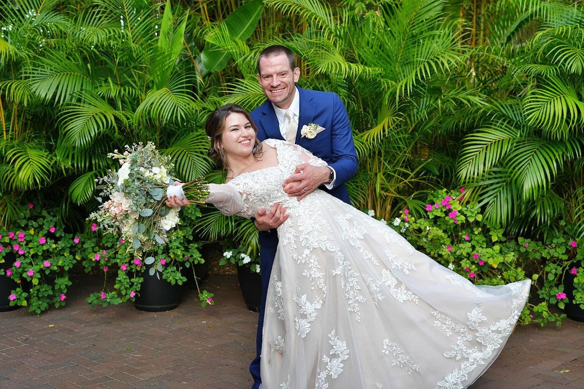 A groom dips his laughing bride in front of lush tropical greenery