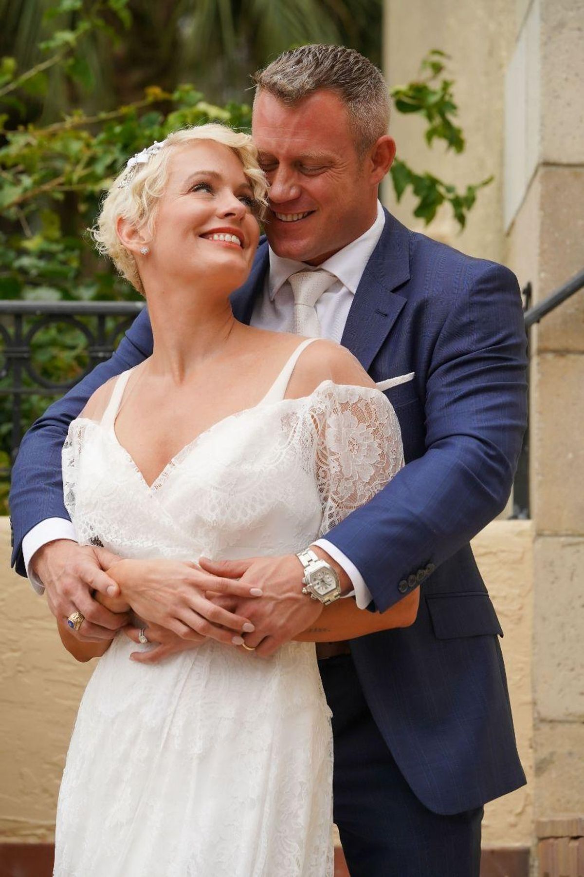 A groom embraces his bride from behind as she smiles up at the sky
