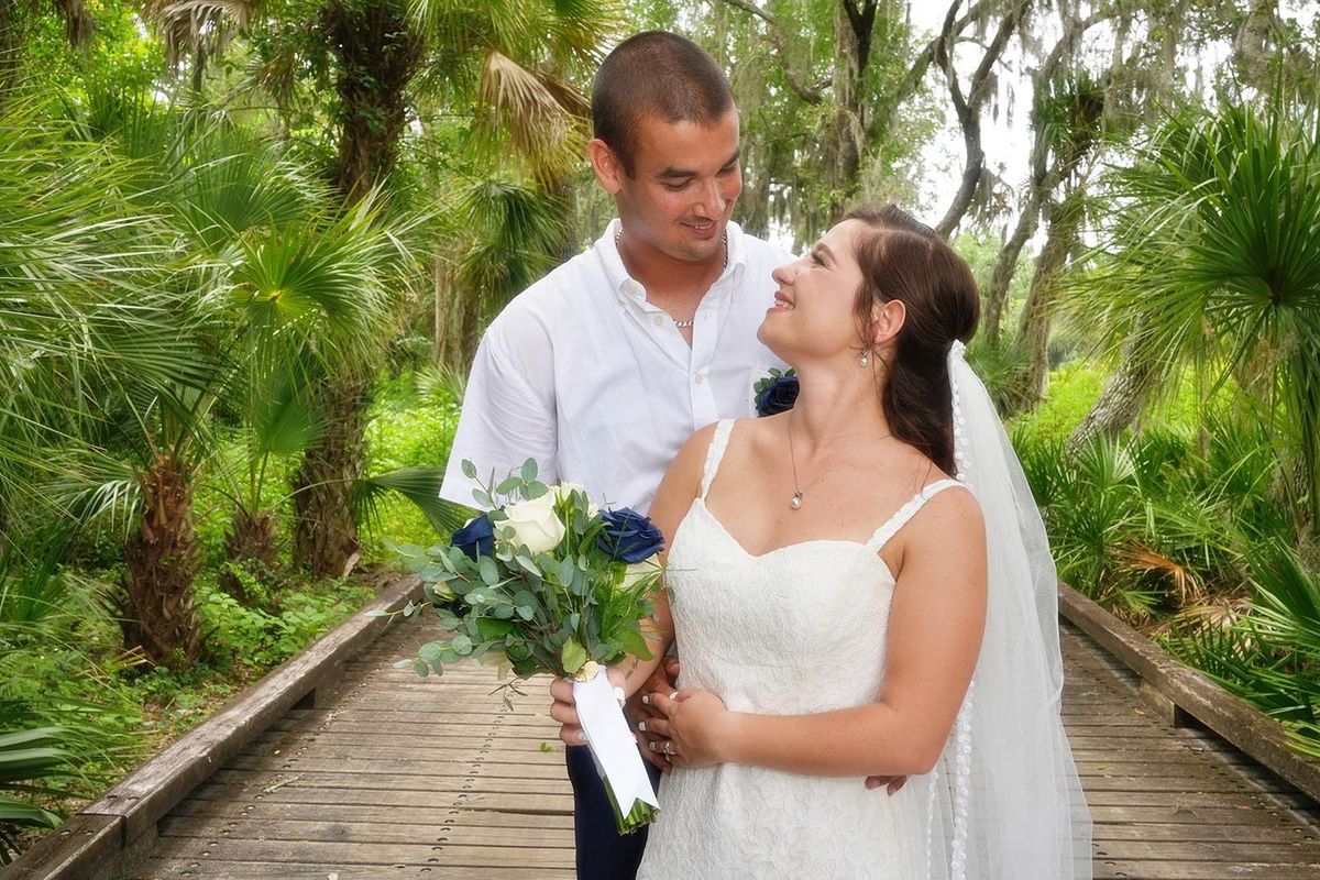 A bride and groom share a quiet look on a boardwalk framed by palms