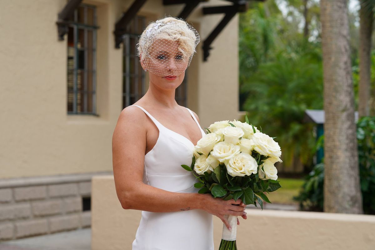 A bride holds a bouquet of white roses outside a historic stucco venue